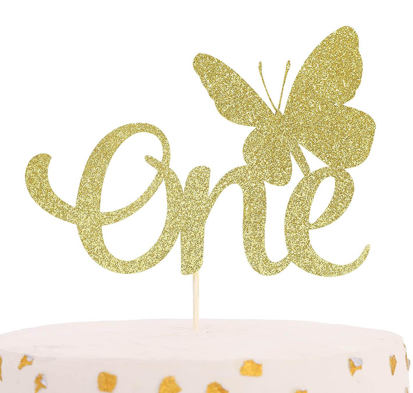 White minimalist cake with gold glitter butterfly and 'One' topper featuring gold leaf accents.