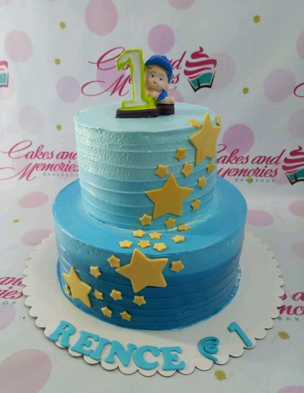 A two-tier blue gradient cake decorated with yellow fondant stars and a baby figurine topper for a first birthday.