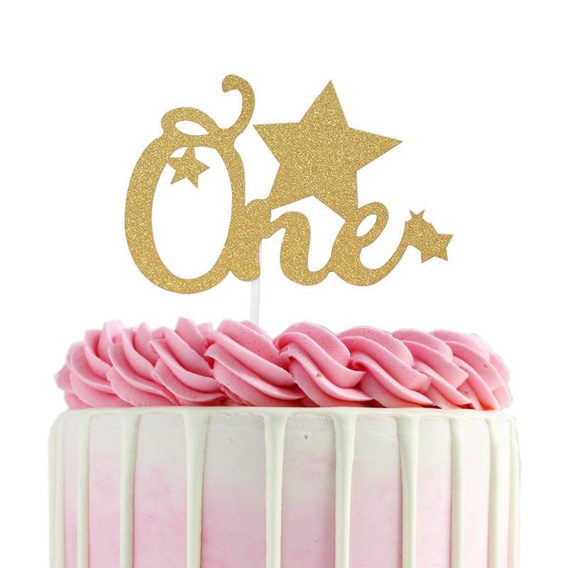 Pink and white ombre cake with white chocolate drip, pink icing rosettes, and a gold glitter 'One' star topper.