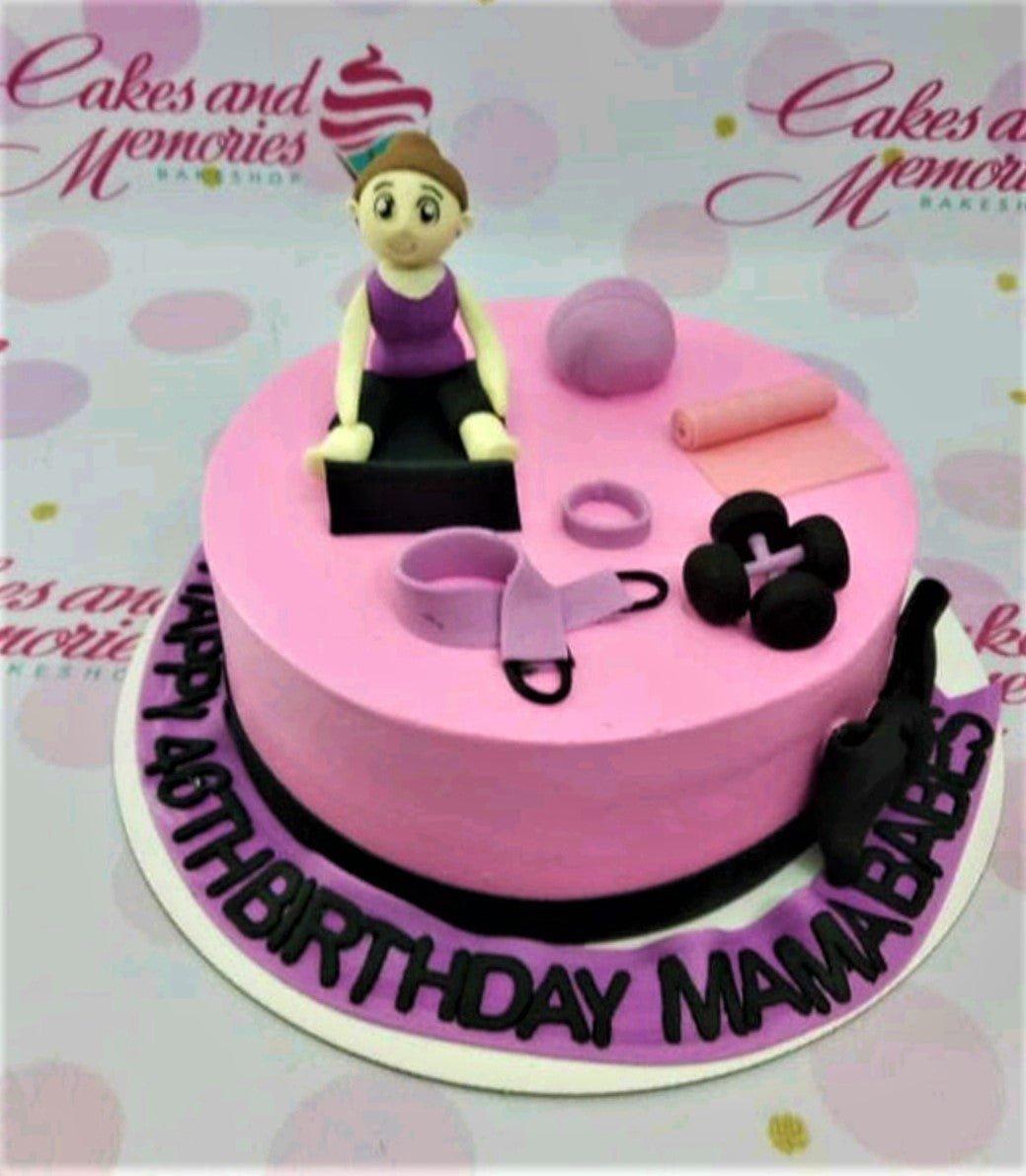 Pink fitness themed birthday cake with a fondant woman figure, dumbbells, yoga mat, and gym equipment on a purple message banner.