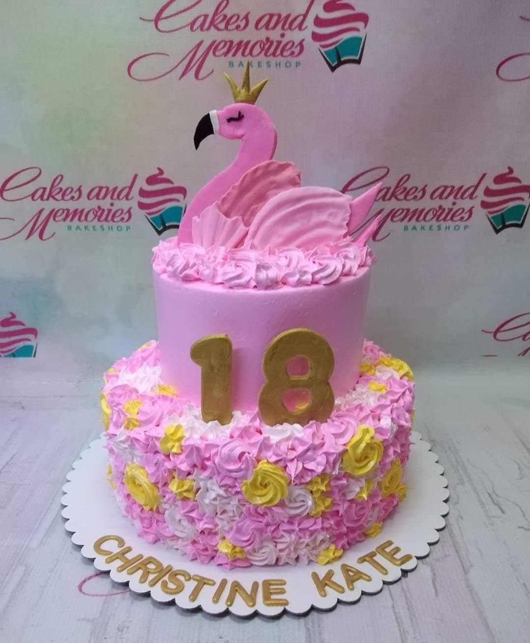 Two-tier pink flamingo birthday cake with pink and yellow icing rosettes and a gold number 18 topper.