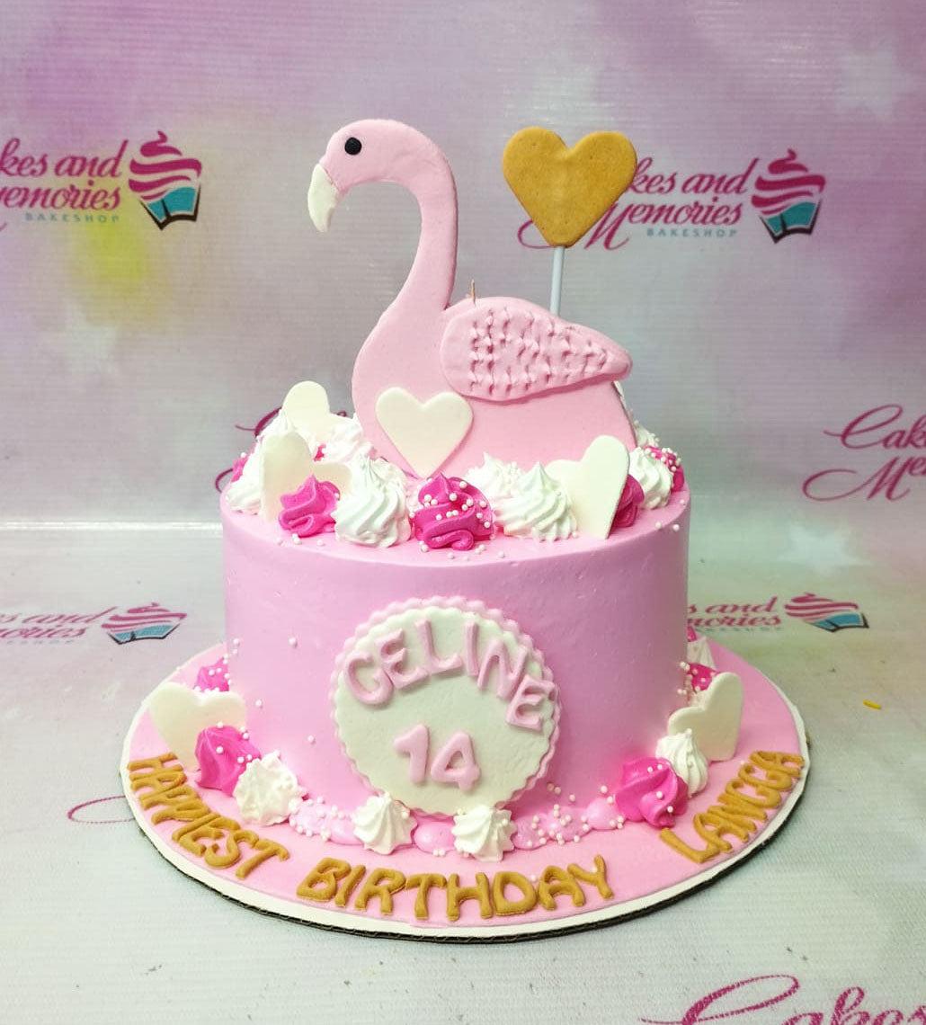 Pink flamingo birthday cake with white and pink icing swirls, heart toppers, and a large pink flamingo fondant figure.
