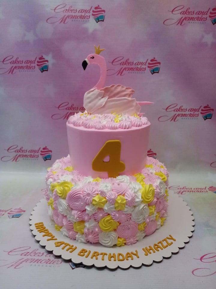 Pink two-tier flamingo birthday cake with yellow and white icing rosettes and a large pink flamingo topper.