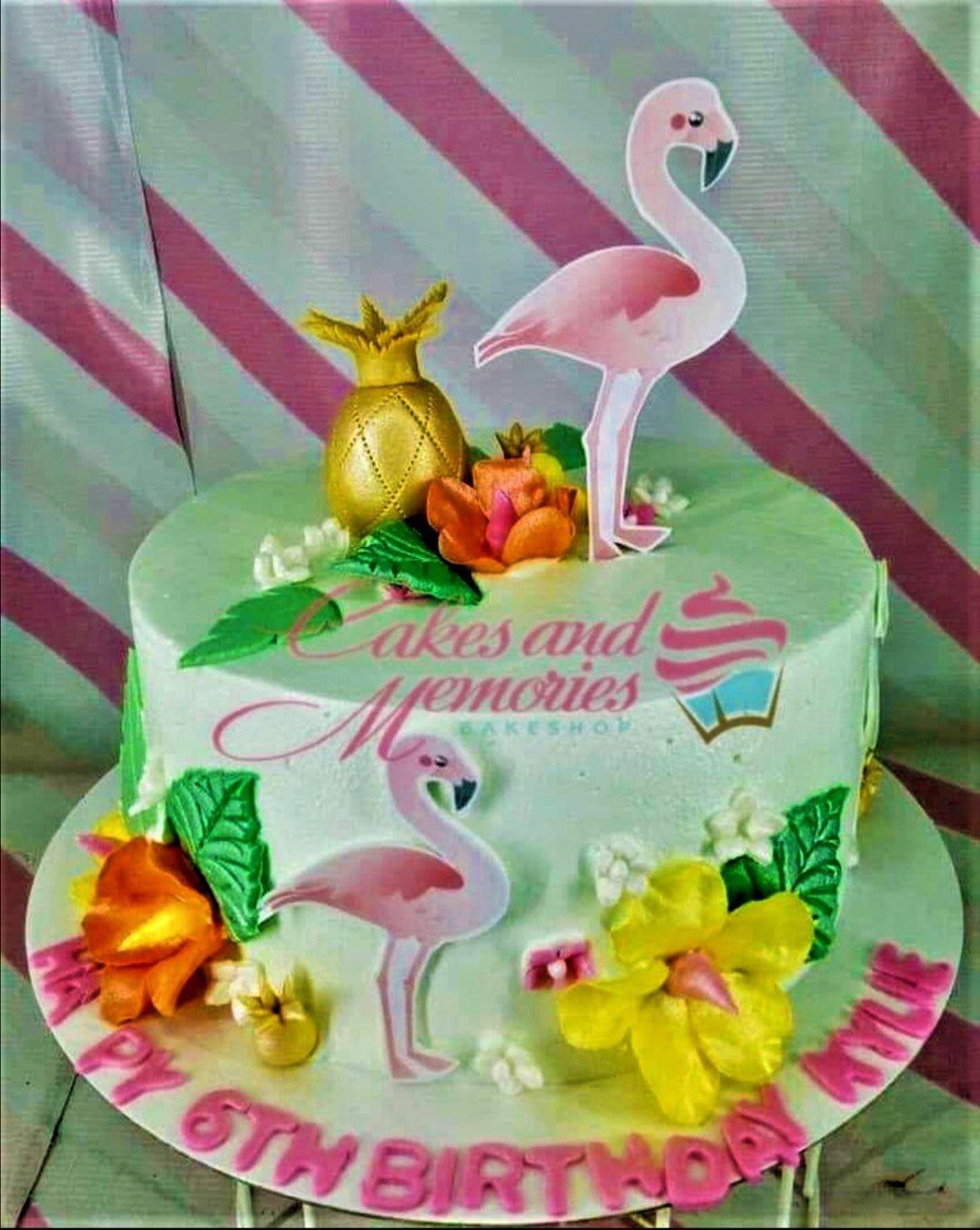Light green tropical flamingo birthday cake with gold pineapple, hibiscus flowers, and pink flamingo printouts.