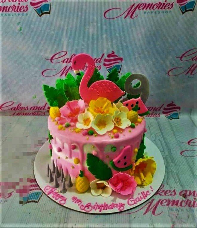Pink flamingo tropical birthday cake with hibiscus flowers, watermelon slices, and a grey number 9 topper.