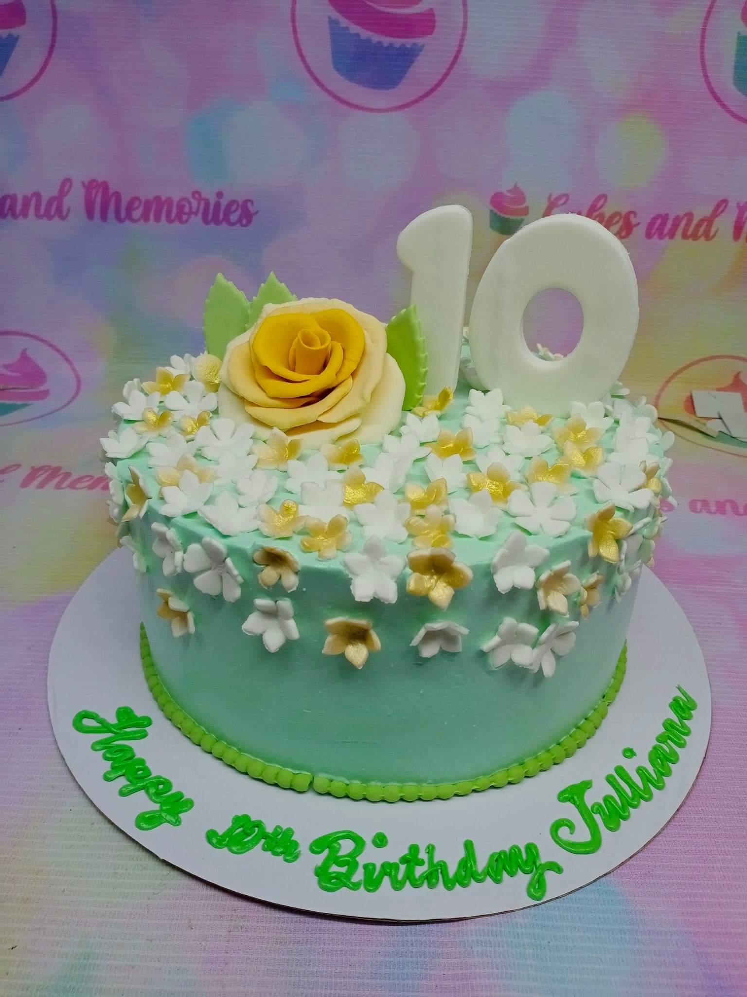 Mint green birthday cake with a large yellow fondant rose, white and gold flowers, and a white number 10 topper.