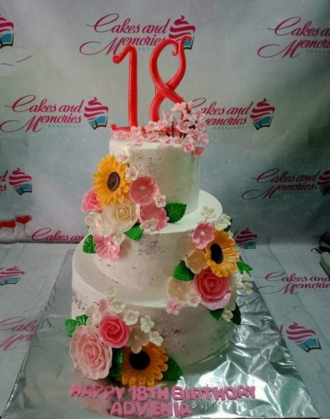 White 3-tier floral birthday cake with pink roses, sunflowers, and a large red number 18 topper.