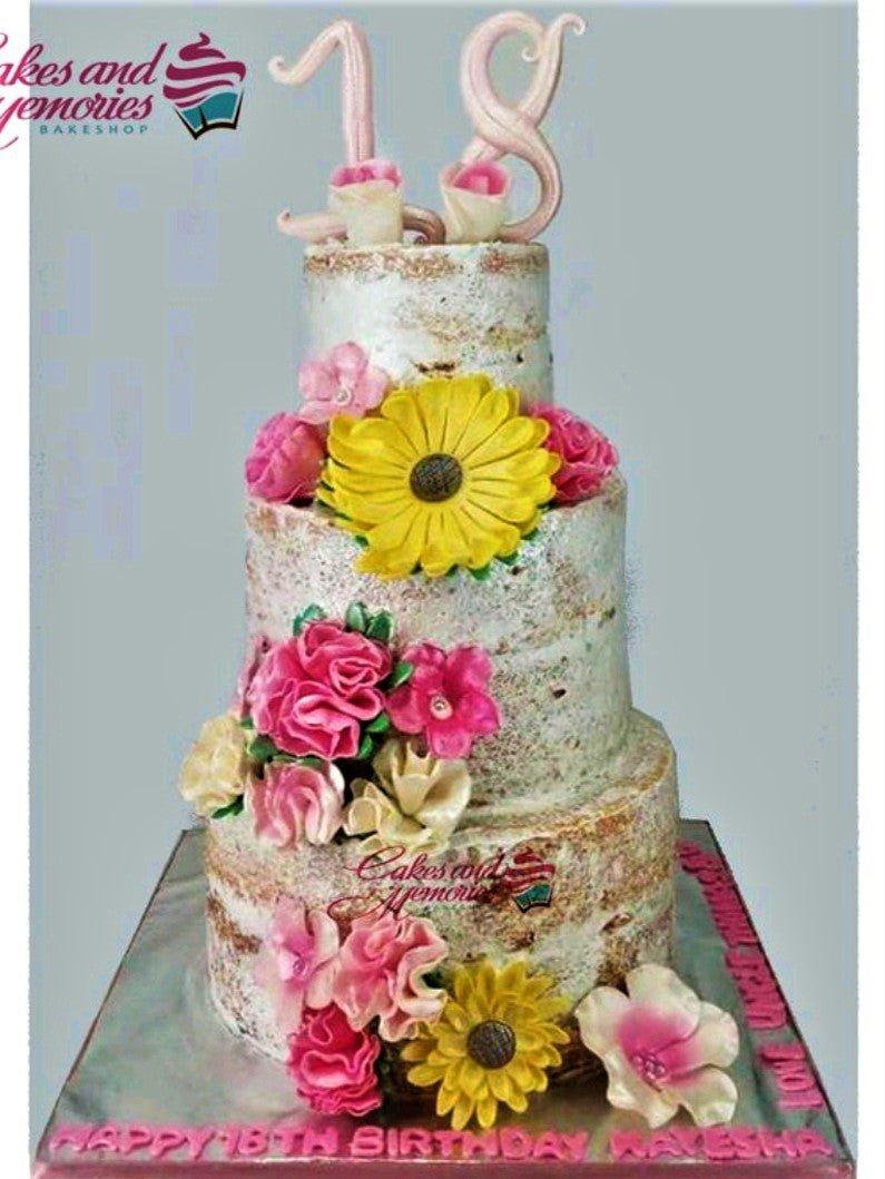 Three-tier semi-naked birthday cake decorated with pink, yellow, and ivory gumpaste flowers and a pink number 18 topper.