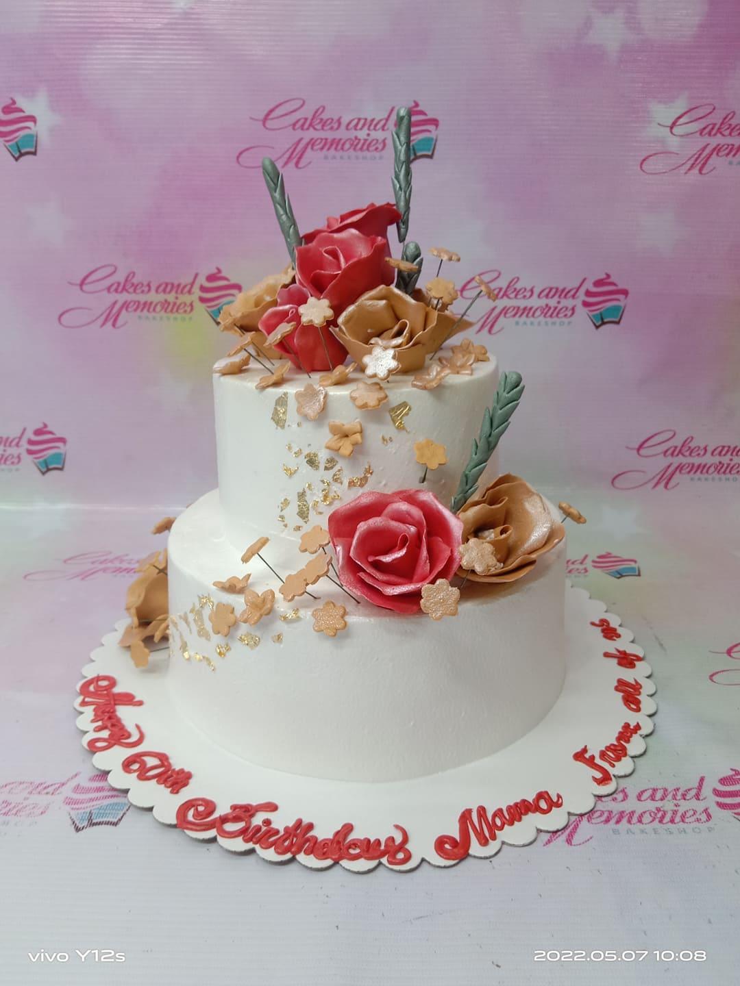 Elegant white 2-tier floral cake with red and gold gumpaste roses, gold leaf accents, and small tan flowers.