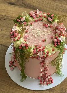 Pink floral garden cake with piped icing rosettes, green moss textures, and gold butterfly accents for a first birthday.