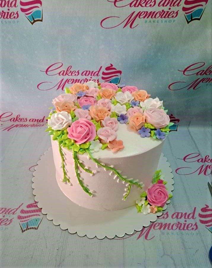 Single tier pink cake covered in a dense arrangement of pink, peach, and white icing roses with green leaves and trailing vines.