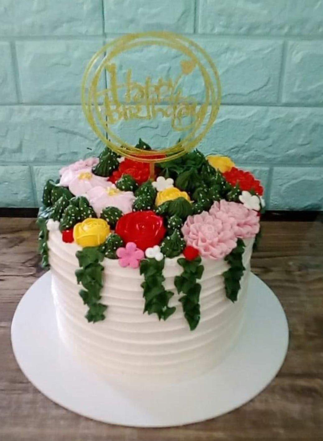 White 1-tier birthday cake with horizontal icing ridges and a lush garden of pink, red, and yellow edible flowers on top.