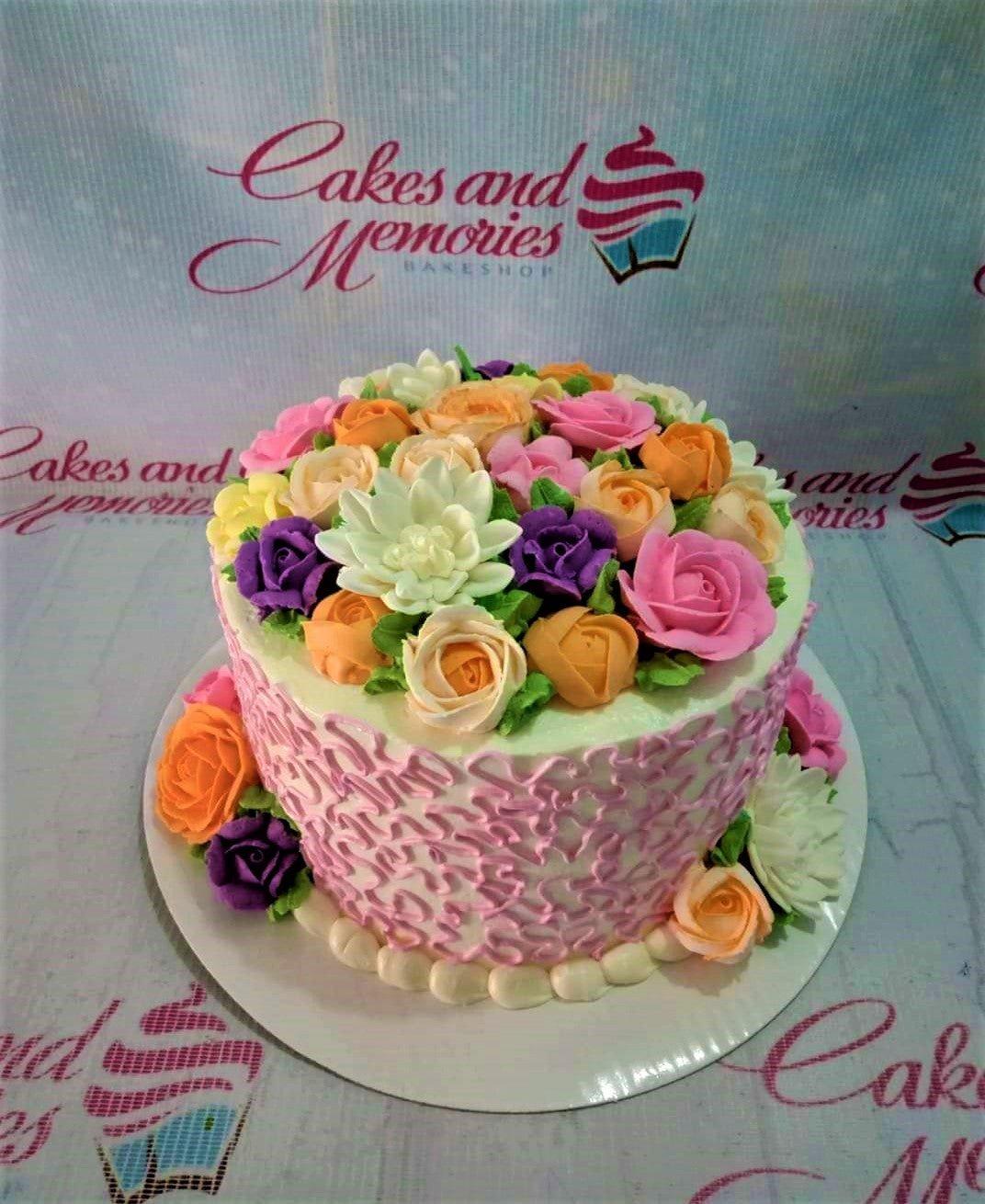 White round cake covered in a dense layer of colorful gumpaste roses in pink, orange, purple, and white with green leaves.