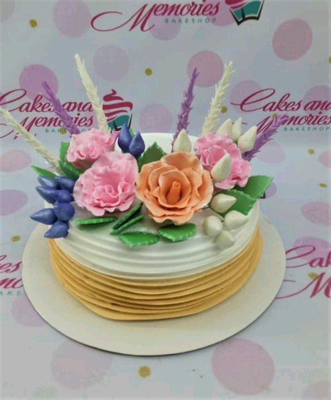 White and peach soft-icing cake decorated with pink and peach edible gumpaste roses and purple lavender-like accents.