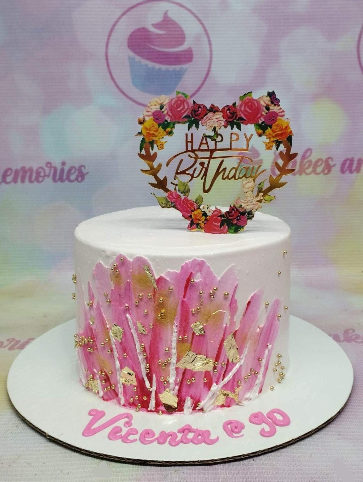 White 1-tier birthday cake with pink palette knife icing strokes, gold leaf accents, gold dragees, and a floral heart topper.