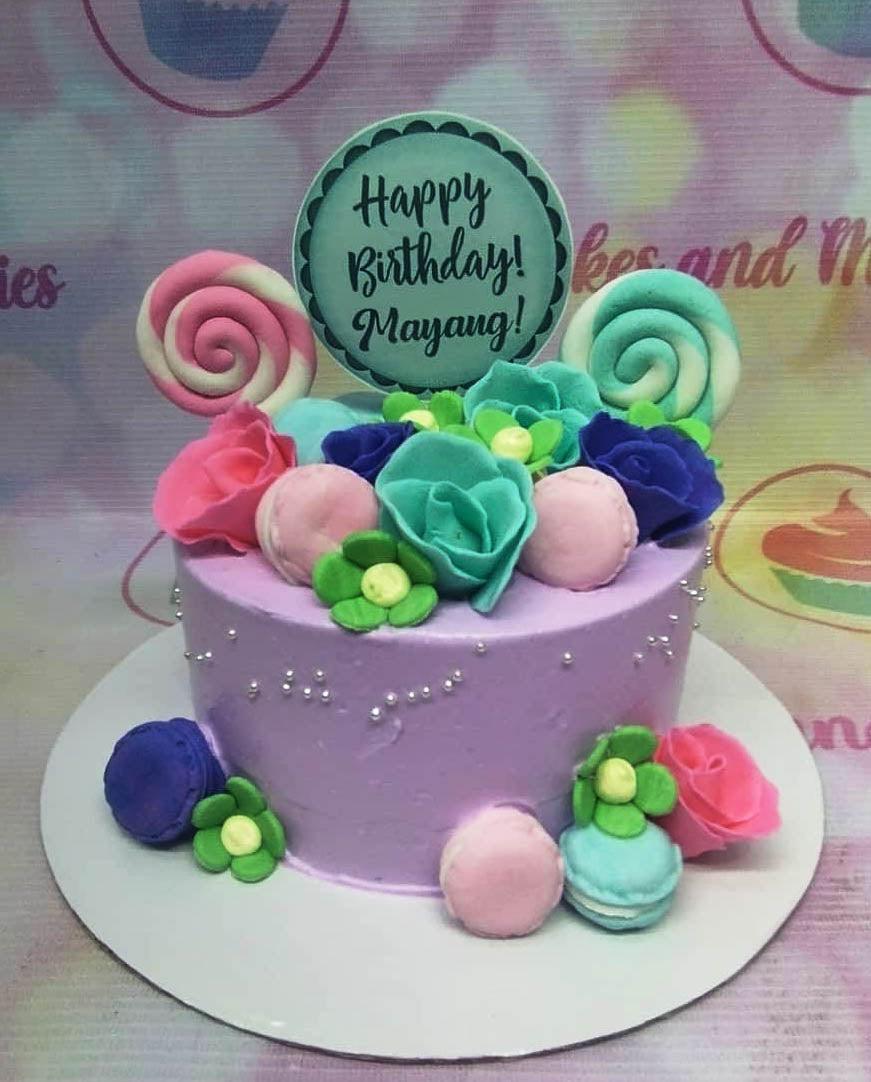 Purple birthday cake with colorful fondant roses, macarons, and lollipops featuring a Happy Birthday Mayang topper.