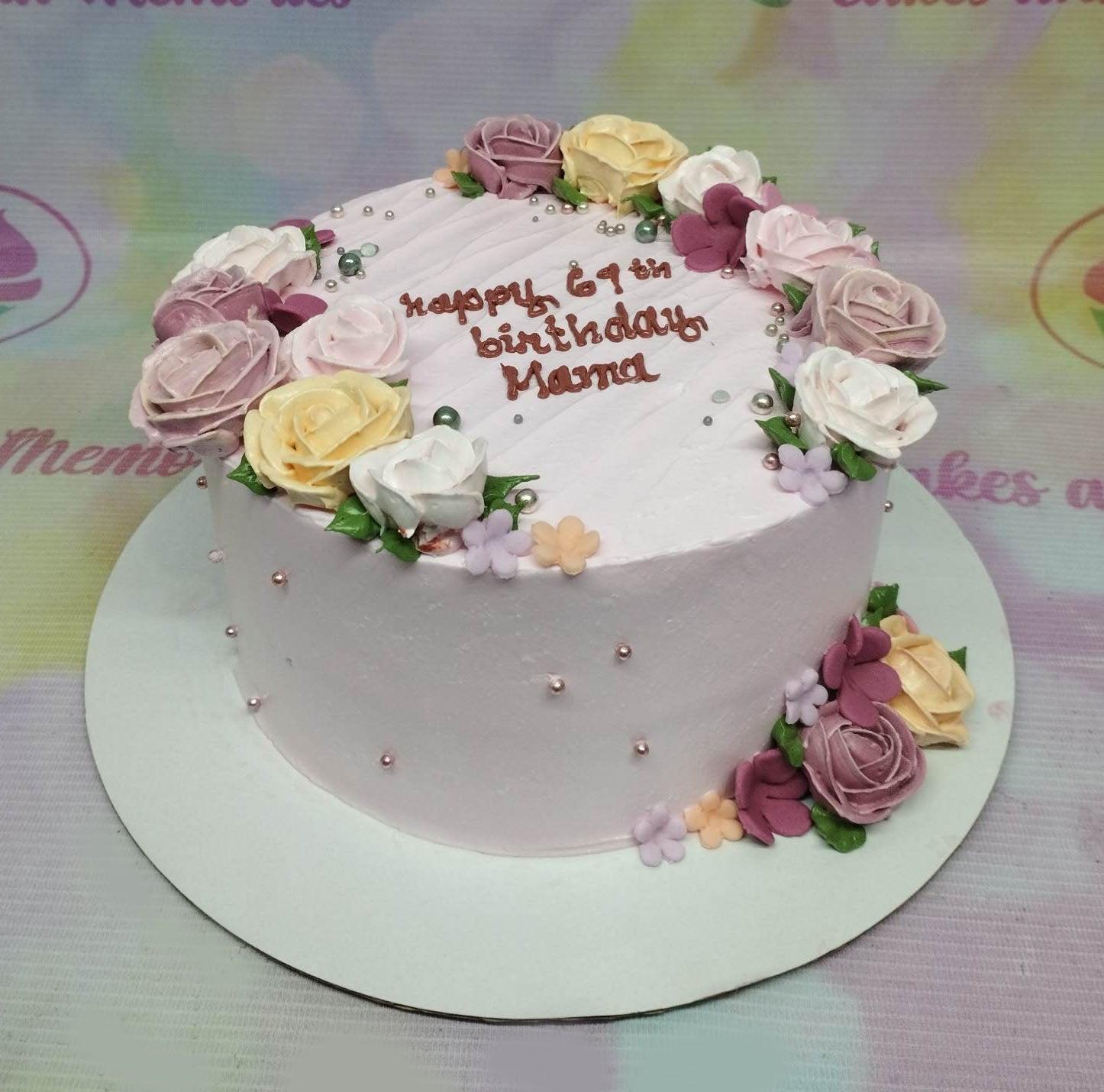 Light purple birthday cake for Mama with piped icing roses in pink, yellow, and white, decorated with silver and green pearls.