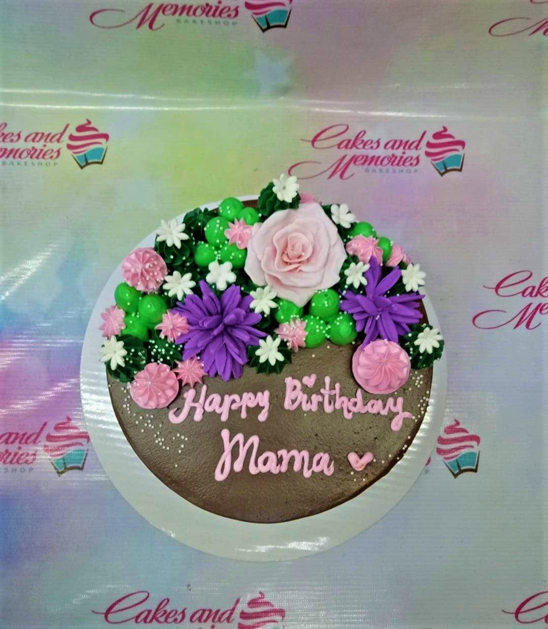 Chocolate birthday cake for Mama decorated with pink, purple, and green icing flowers and white rosettes.