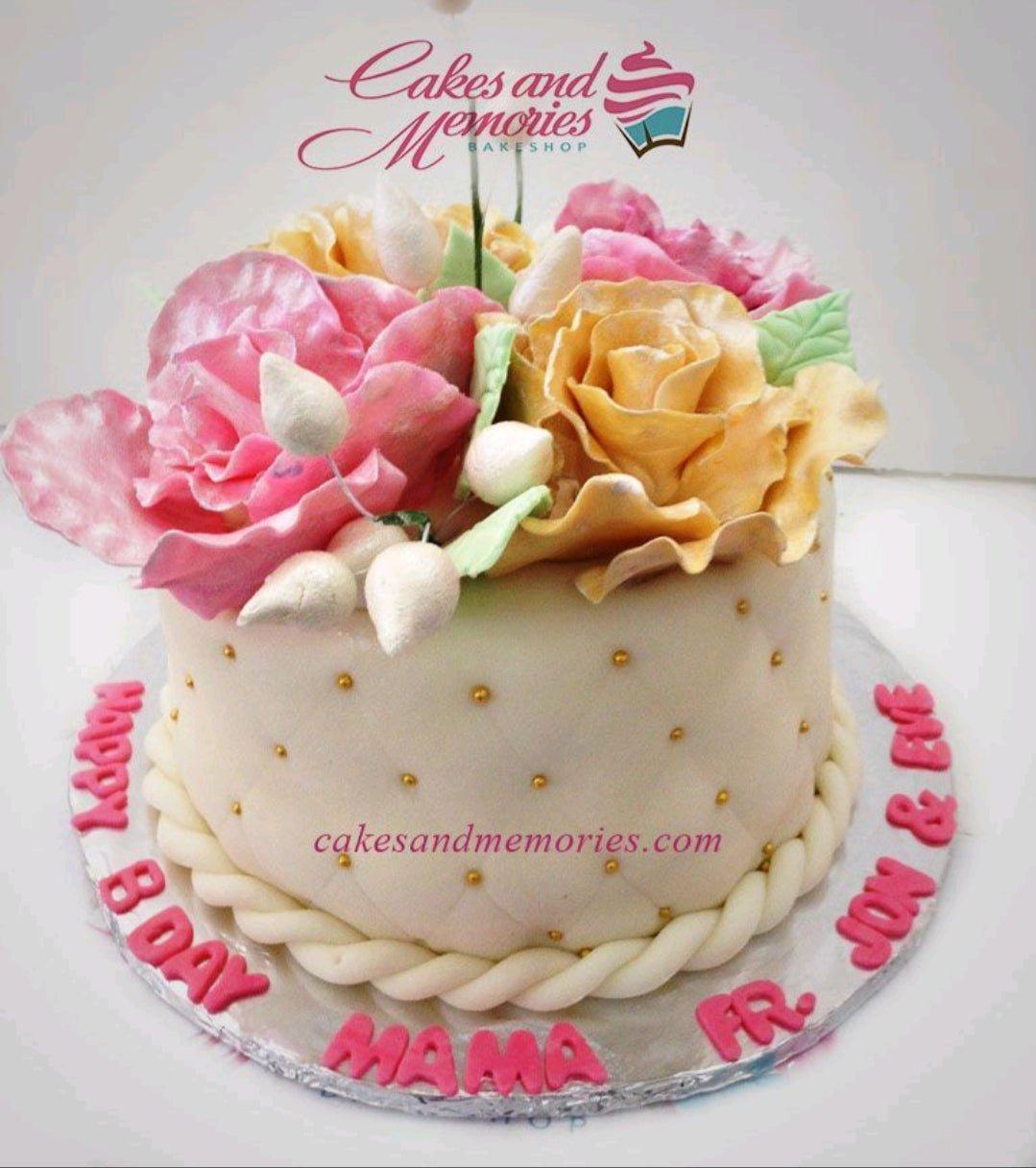 Elegant white fondant cake with large pink and yellow gumpaste roses, gold dragees, and a twisted rope border.