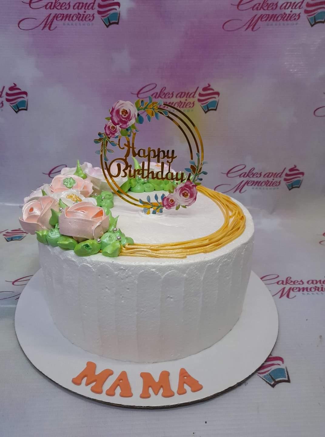 White textured icing cake with pink and white icing roses, green leaves, and a gold Happy Birthday topper for Mama.