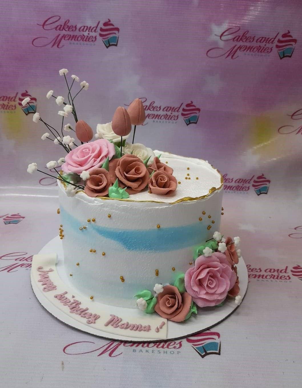 White and blue soft icing cake decorated with pink and brown gumpaste roses and gold dragees.
