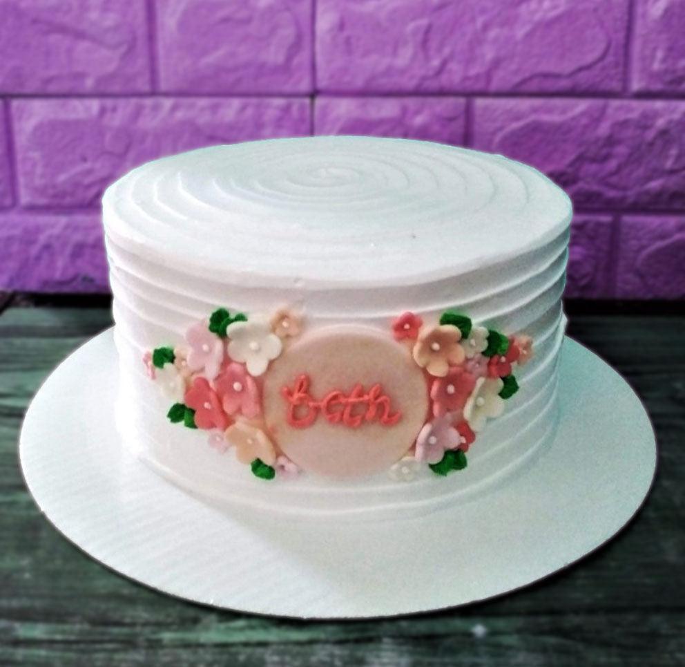 White minimalist cake with horizontal icing ridges and a central floral gumpaste plaque featuring the name Beth in pink script.