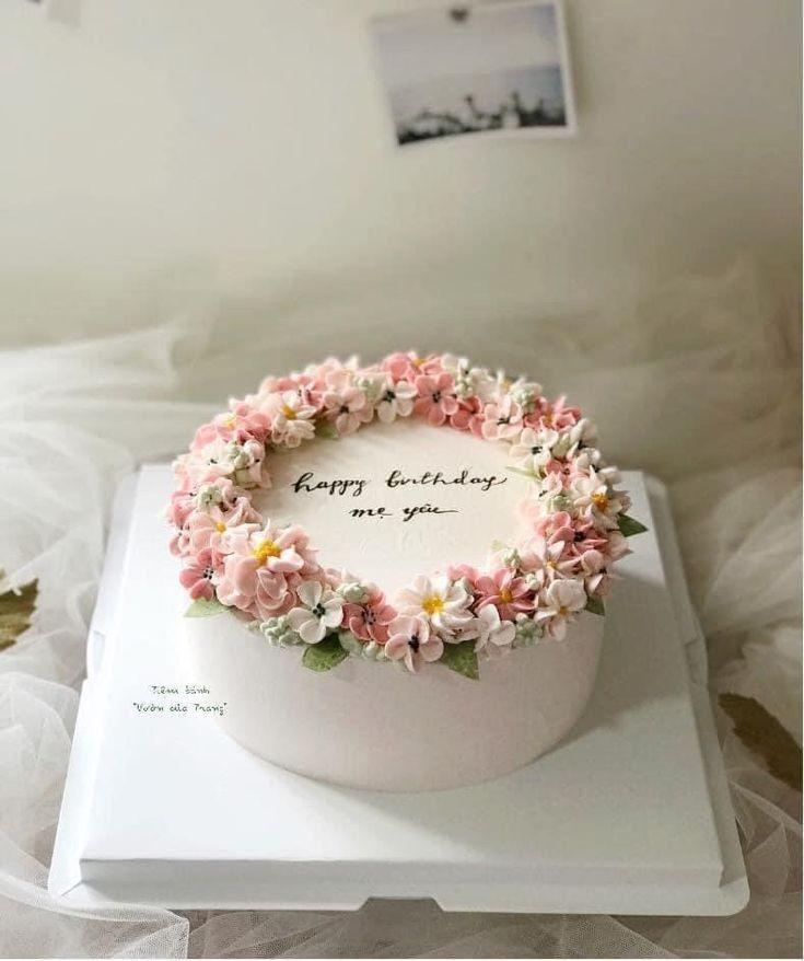White minimalist birthday cake with a wreath of pink and white piped icing flowers and green leaves.