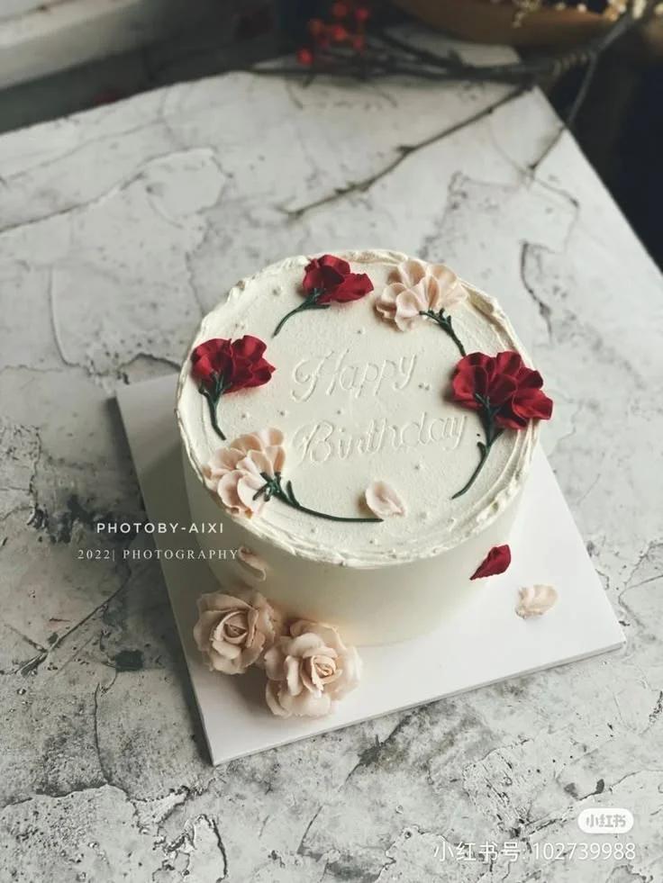 White minimalist birthday cake with red and peach gumpaste carnations and piped icing Happy Birthday message