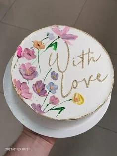 White bento cake with palette knife painted purple and pink flowers and gold icing text reading With Love