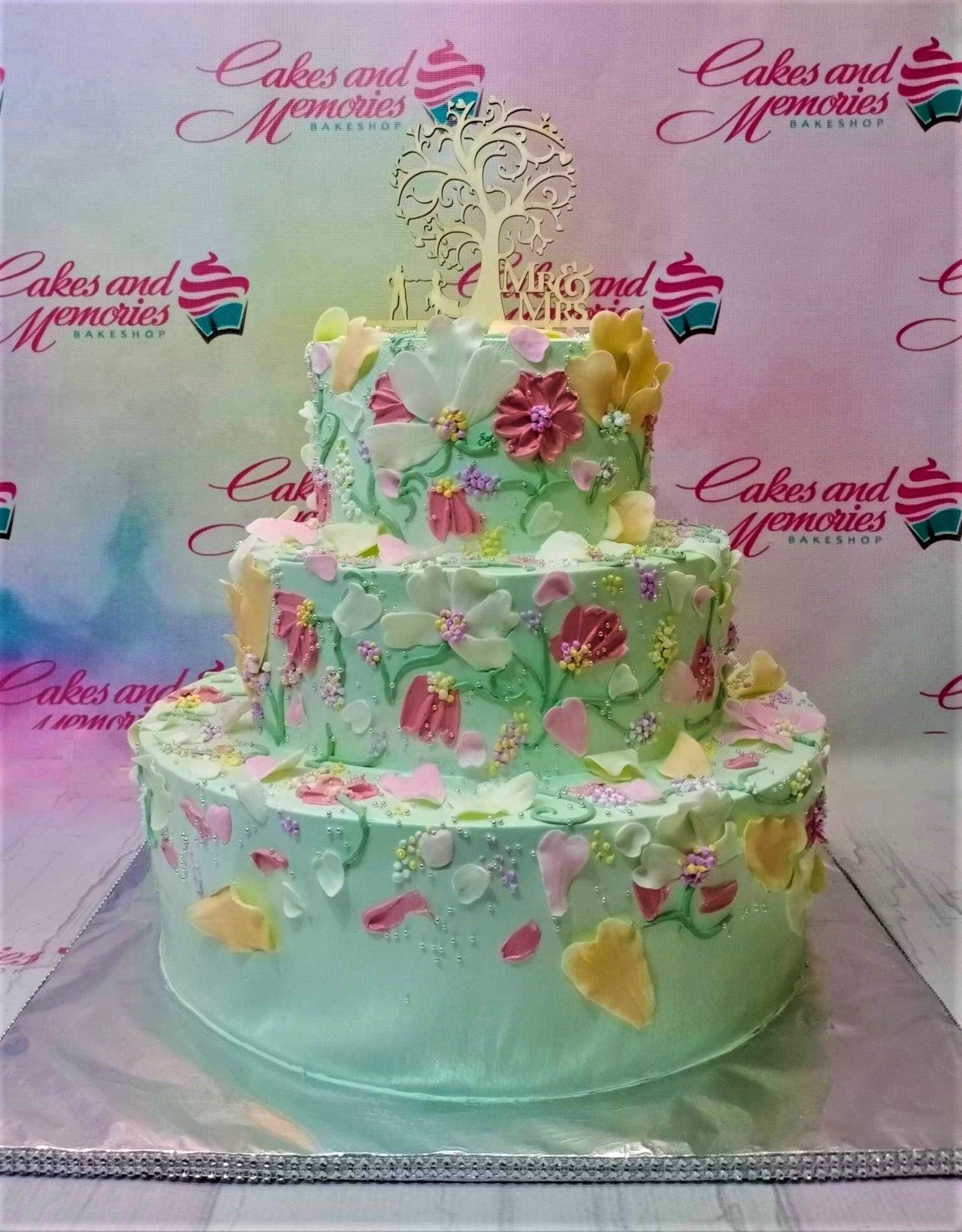 Three-tier mint green cake with intricate palette knife floral designs in pink, white, and yellow, topped with a wooden tree topper.