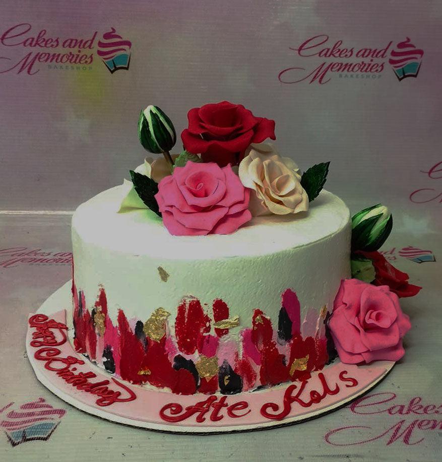 White round cake with pink and red palette knife icing strokes, gold leaf accents, and topped with pink, red, and cream gumpaste roses.
