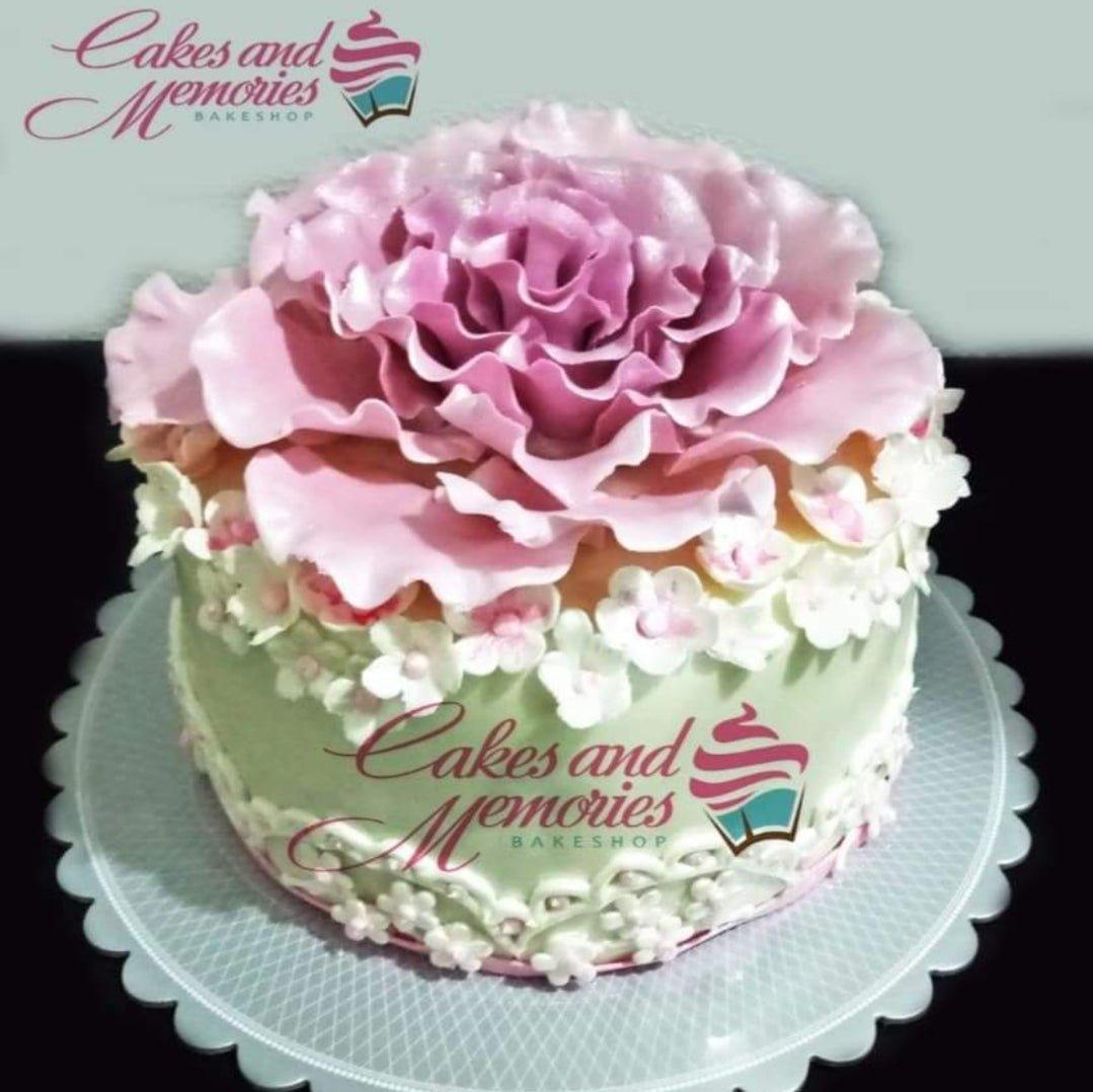 Light green single tier cake topped with a large pink gumpaste peony and surrounded by small white and pink flowers.