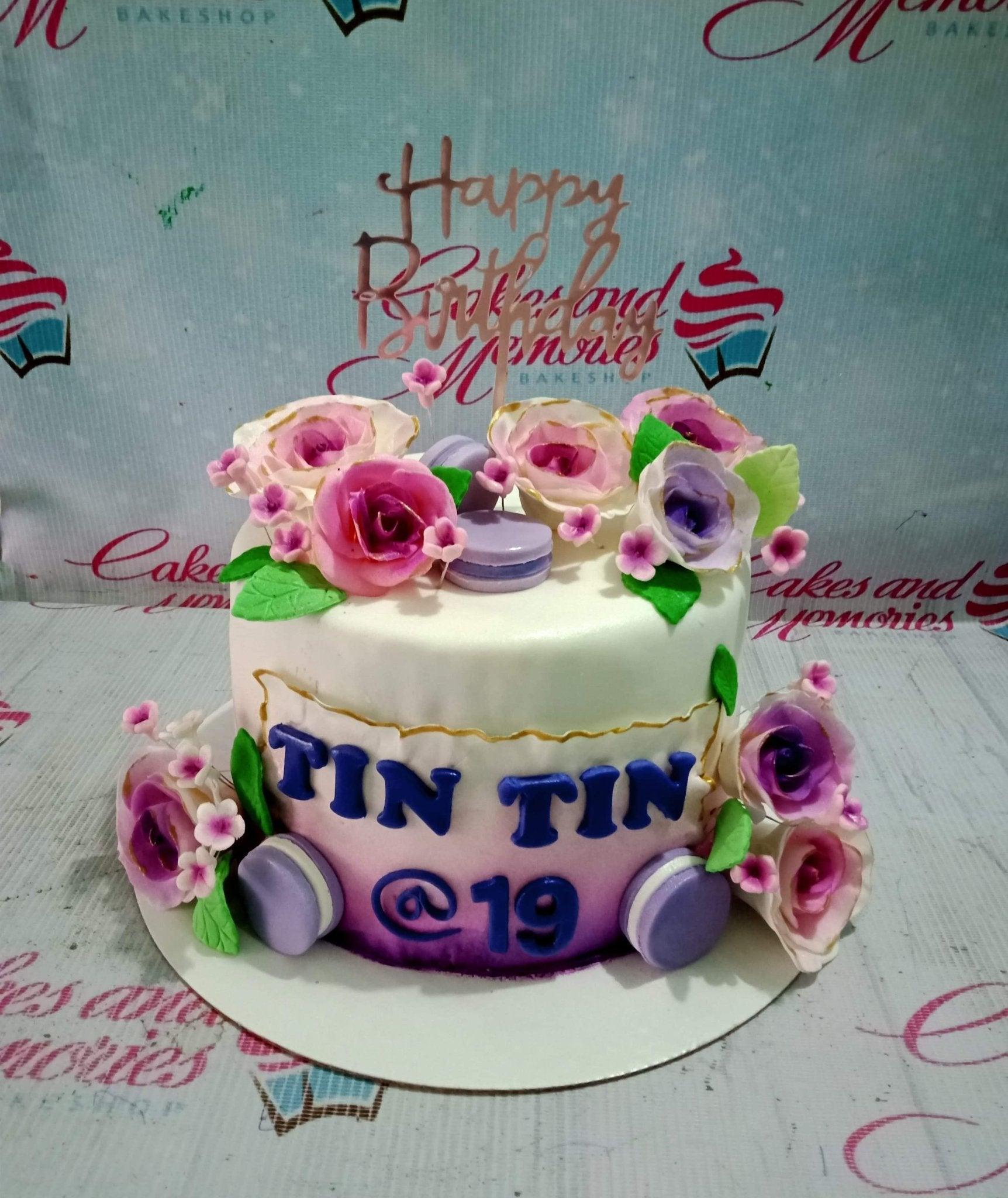White and purple gradient fondant cake with pink and purple sugar roses, macarons, and a rose gold Happy Birthday topper.