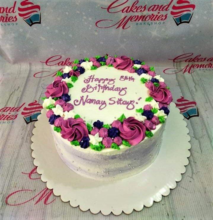 White round birthday cake with purple and pink icing rosettes, green leaves, and silver dragees for Nanay Sitang's 85th birthday.
