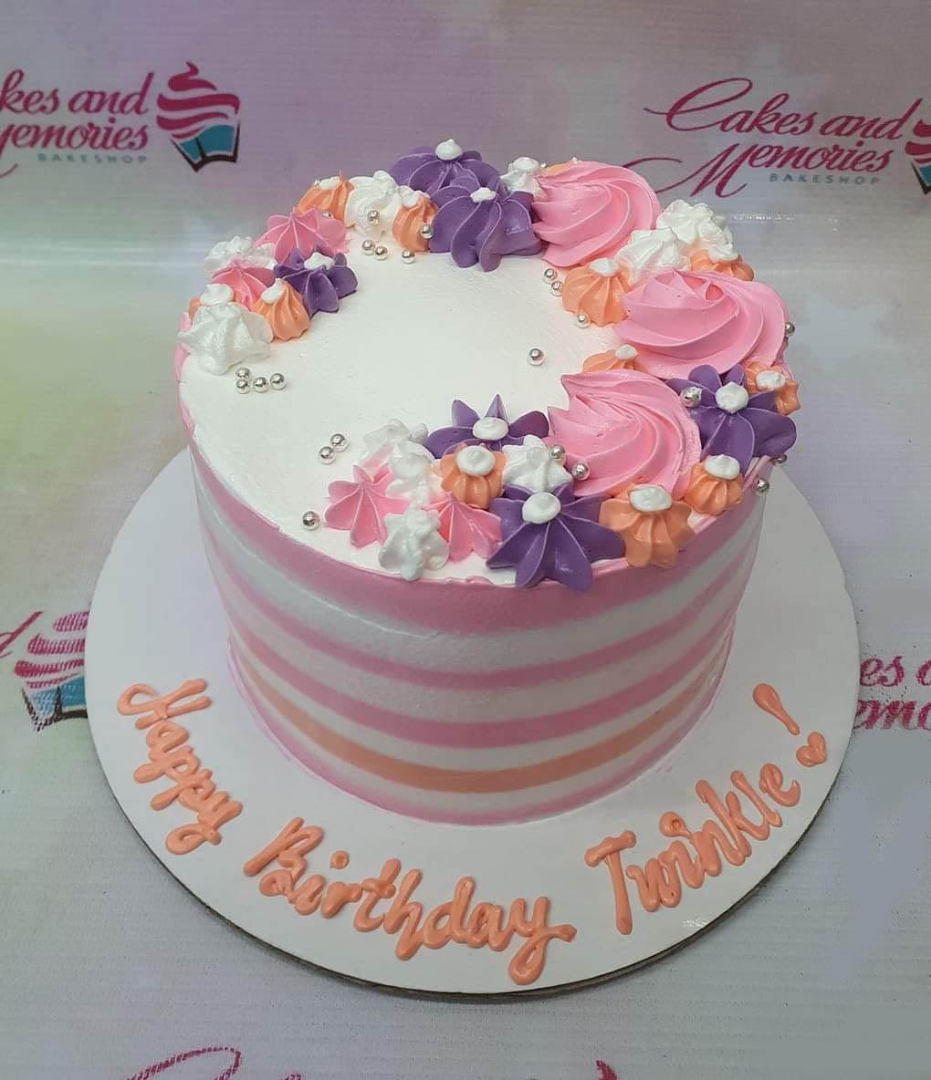 White and pink striped birthday cake with purple, pink, and orange icing rosettes and silver dragees.