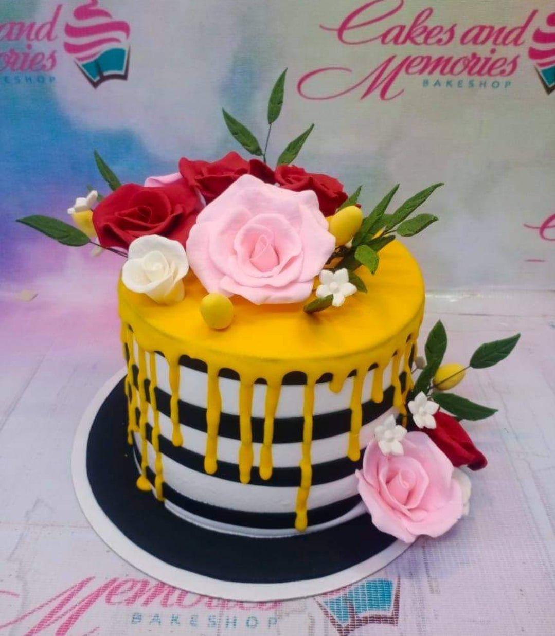 Black and white striped cake with yellow drip and pink and red gumpaste roses on top and side.