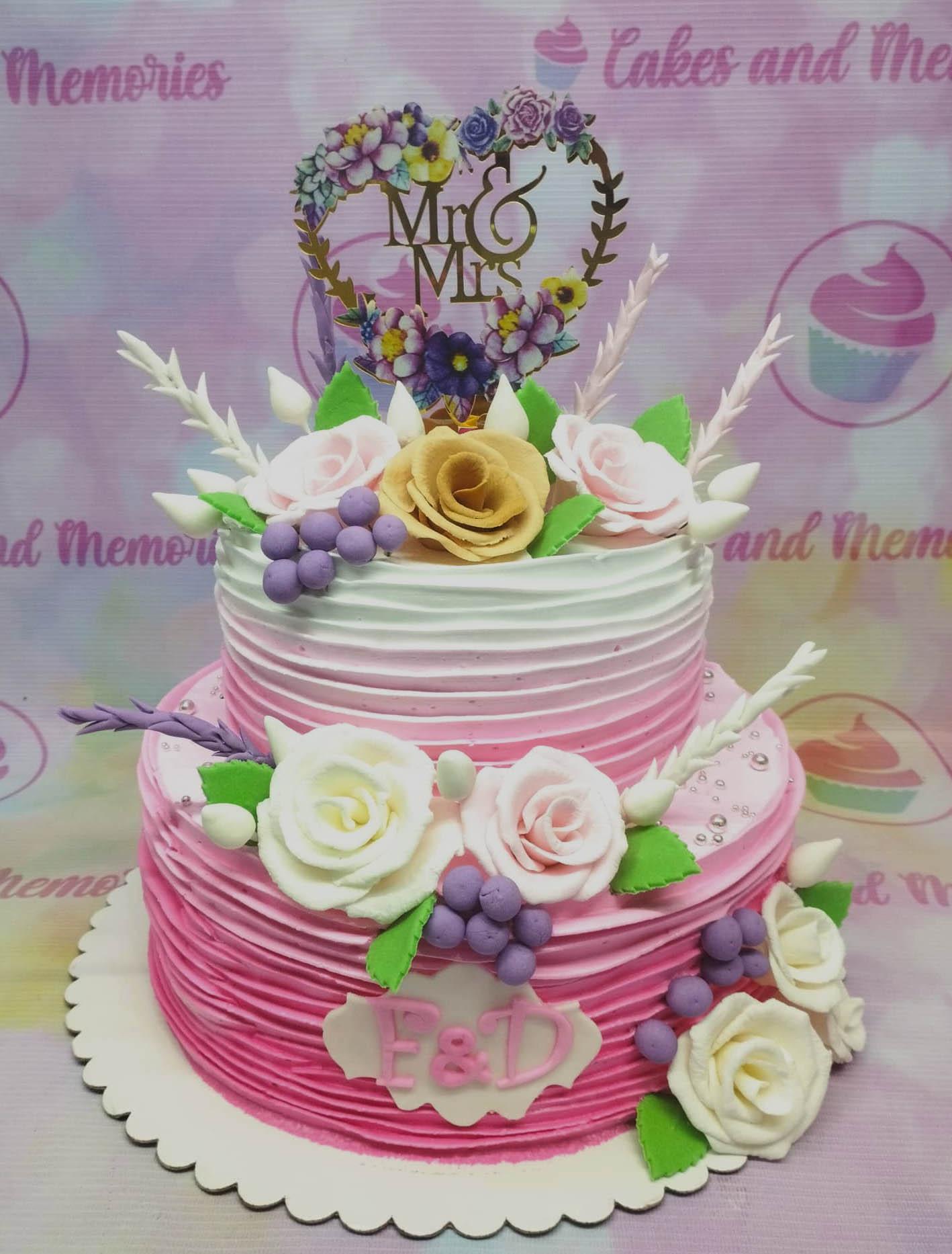 Two-tier pink and white ombre cake with horizontal icing ruffles, gumpaste roses, and a floral Mr & Mrs heart topper.