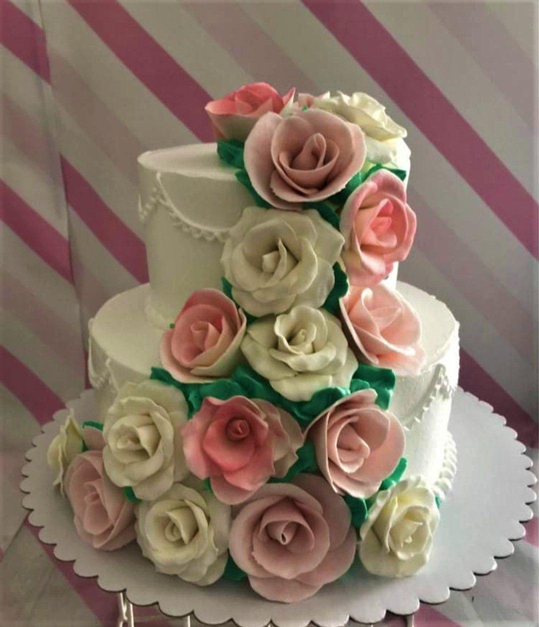 Elegant two-tier white cake adorned with a cascading floral arrangement of pink and white gumpaste roses and green leaves.