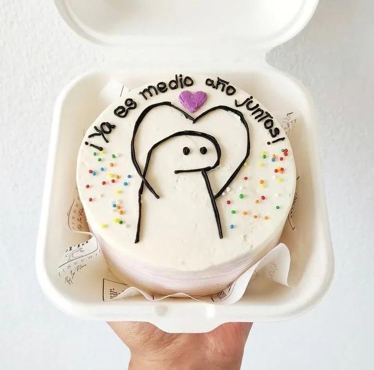 White bento cake with a hand-drawn black icing Flork character holding a purple heart and colorful sprinkles.