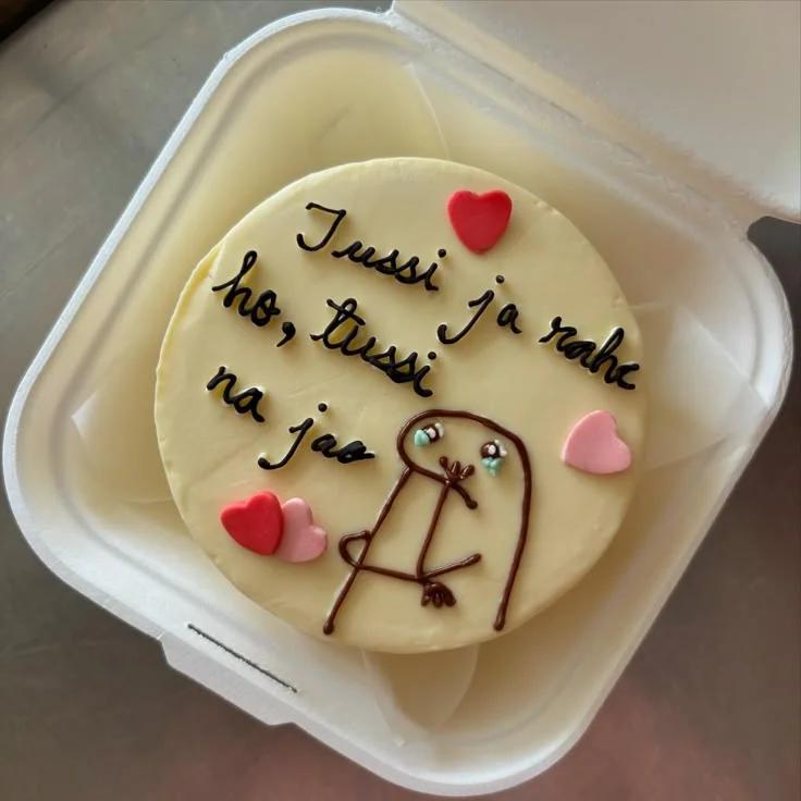 White bento cake with a hand-drawn crying Flork character and pink and red hearts, featuring a funny message in Hindi.