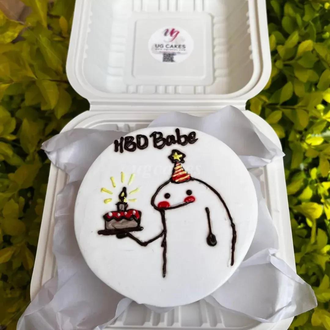 White bento cake with a hand-drawn Flork character holding a small birthday cake and wearing a party hat.