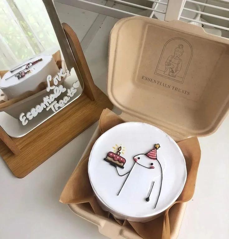 White bento cake in a kraft box featuring a hand-drawn minimalist Flork character wearing a party hat and holding a small cake.