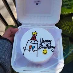 White bento cake with a hand-drawn Flork character wearing a party hat and holding balloons, with Happy Birthday text.