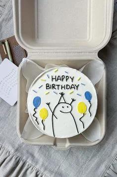 White bento cake with a hand-drawn minimalist character holding balloons and a Happy Birthday message.