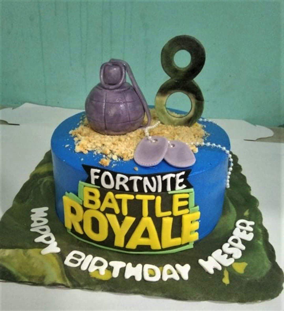 Blue Fortnite Battle Royale themed birthday cake with a purple grenade, dog tags, and camouflage base board.