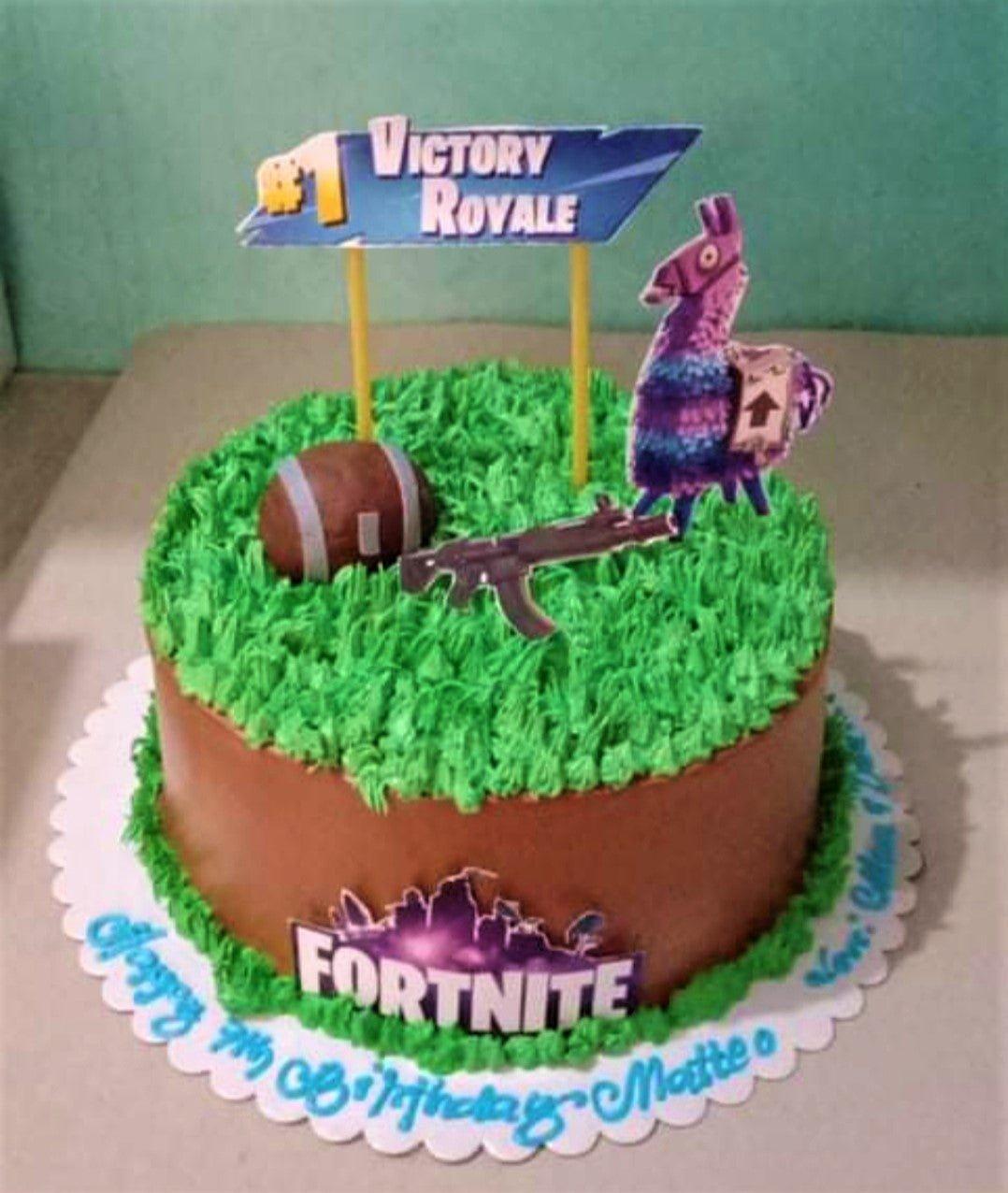 Fortnite themed birthday cake with brown icing, green grass-like piping, and various game-related printout toppers.