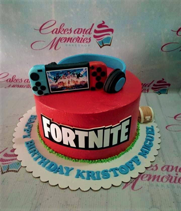 Red Fortnite themed birthday cake with a Nintendo Switch and headset topper on a green grass border.
