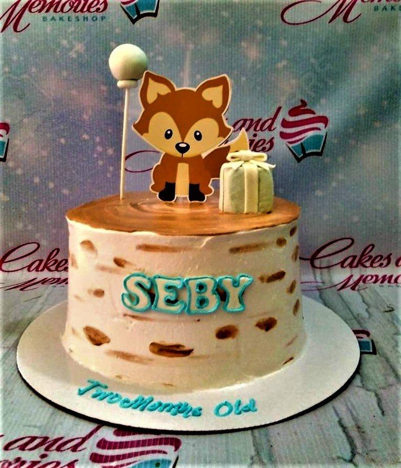 A rustic birch wood log cake with a cute fox printout topper and a small fondant gift box for a two-month-old celebration.