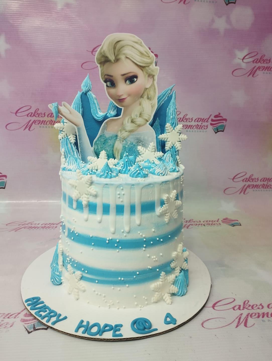 Frozen Elsa themed birthday cake with blue and white striped icing, white snowflakes, and a large Elsa printout topper.