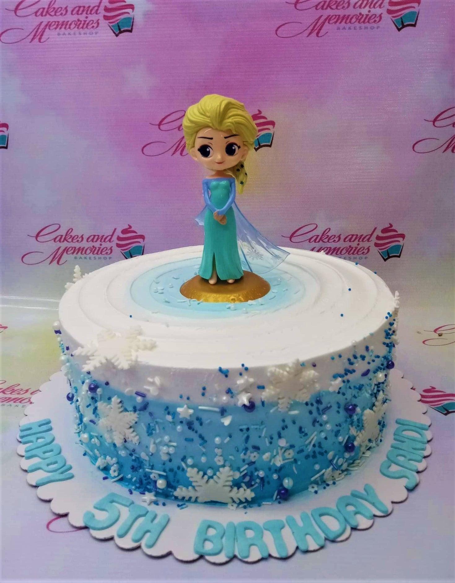 Frozen Elsa themed birthday cake with blue and white gradient icing, snowflakes, and a 3D Elsa figurine on top.